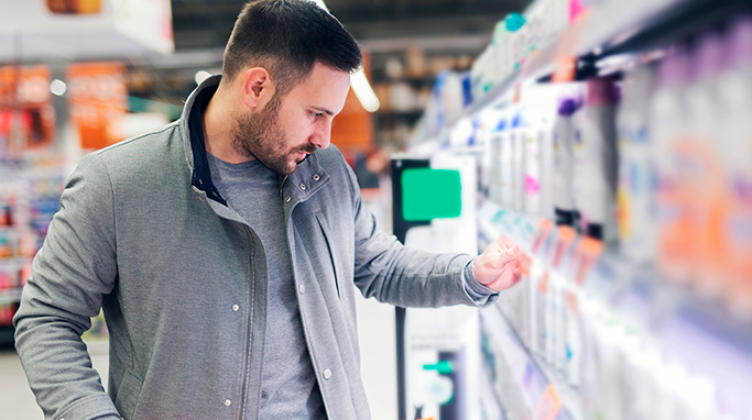 Mand overvejer hvilken shampoo han skal vælge i butikken